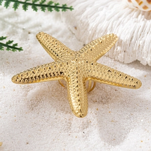 Exaggerated golden starfish ring with textured metallic finish on white beach sand