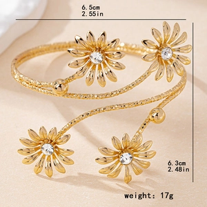 Elegant gold daisy arm cuff with spiral design and sparkling crystals on stone background