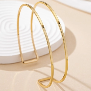 Close-up of polished gold adjustable minimalist coil arm cuffs on textured base