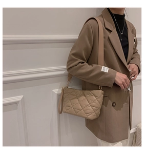 Quilted khaki shoulder bag with gold hardware and wide strap on camel suit model