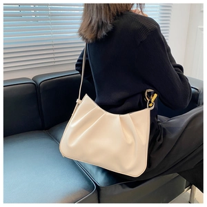 Chic beige pleated cloud bag shown on shoulder with metal chain detail in minimalist scene