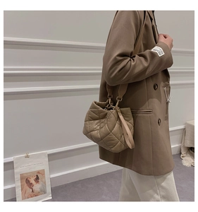 Quilted khaki bucket bag with plush padding worn on shoulder by model in a suit