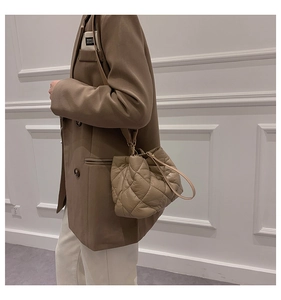 Detail of a beige quilted drawstring bucket bag with gold hardware worn by a model