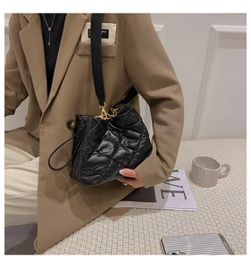 Side view of a black quilted bucket bag with golden hardware and wide strap shown on model