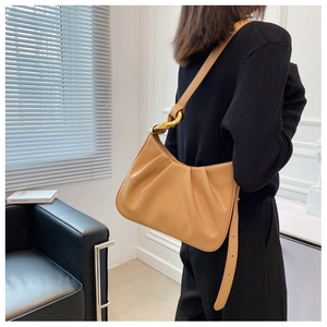 Detail of light brown pleated leather shoulder bag with bold gold chain link accents