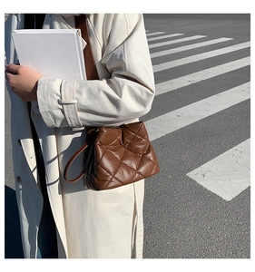 Outdoor shot of a brown quilted leather bucket bag worn with a white trench coat