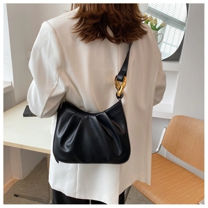 Detail of black leather pleated bucket bag featuring a decorative gold chain shoulder strap