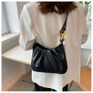 Detail of black pleated cloud bag with chunky gold chain on white blazer