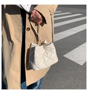 Quilted cream bucket bag held by a model in a trench coat on a street background