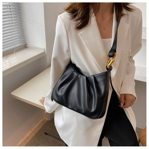 Close-up of black pleated cloud bag with chunky gold chain hardware on a model