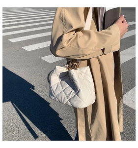 Fashionable white quilted bucket bag shown with a khaki trench coat on a city street