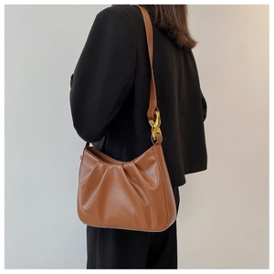 Close-up of caramel pleated cloud bag with chunky gold chain detail on a black blazer
