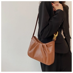 Detail of brown pleated cloud bucket bag with chunky gold chain strap on black blazer