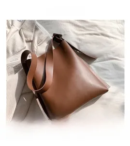 Detailed view of the large brown PU leather tote bag on a textured white fabric backdrop
