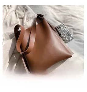 Detail of a large brown leather tote bag with a wide strap on a soft white fabric surface