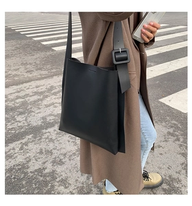 Detail of minimalist black leather tote bag with wide strap and square buckle on model