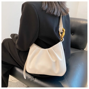 Detail of cream pleated cloud bag with large golden chain buckle on a model's shoulder