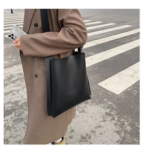 Side view of a large black leather tote bag worn by a person on an urban street