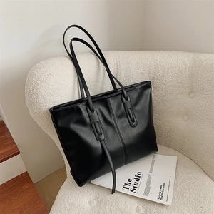 Large black faux leather tote bag with long straps on a white fleece sofa background