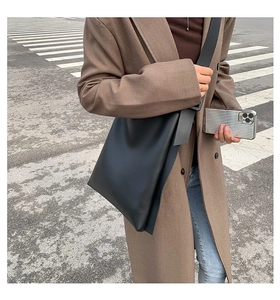 Chic black leather tote bag with wide strap worn by woman on urban street setting