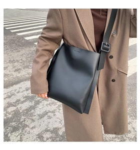 Minimalist black tote bag with wide strap and square buckle on model in city street