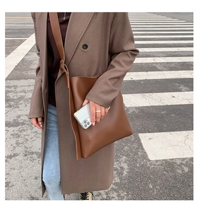 Brown large capacity tote bag shown in outdoor street style with wide crossbody strap