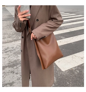Street style shot of a large brown leather tote bag with long strap and matte finish