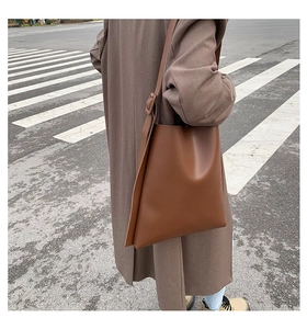 Street view showing side profile of large brown leather tote bag on model shoulder