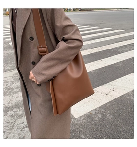 Brown leather tote bag styled on model with a long coat on a city street crossing