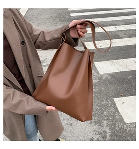 Detail of large brown tote bag in matte leather shown in a street style setting