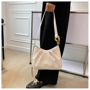 Close-up of beige ruched dumpling bag with elegant gold geometric shoulder strap hardware