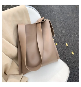 Close-up of beige leather tote bag featuring a wide shoulder strap and square buckle detail