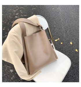Close-up of minimalist clay leather tote bag with wide shoulder strap on a beige blazer