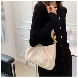 Detail of off-white pleated cloud bucket bag with chunky gold chain strap worn on shoulder