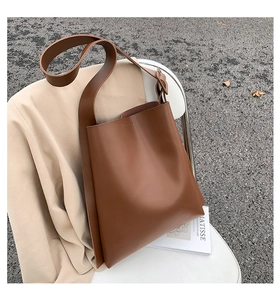 Detail of a brown matte leather tote bag with wide straps on a stylish chair
