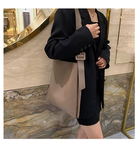 Close-up of earth-toned leather tote bag showing wide shoulder strap and square buckle detail