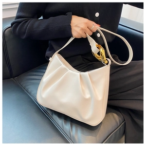 Close-up of pleated beige bucket bag featuring a large gold chain buckle on shoulder strap