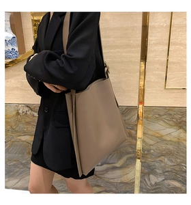 Side view of a large taupe PU leather tote bag with wide strap worn by a model