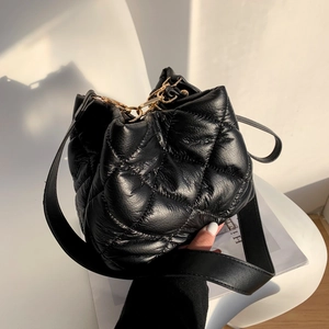 Quilted black bucket bag with gold hardware and wide shoulder strap in lifestyle setting