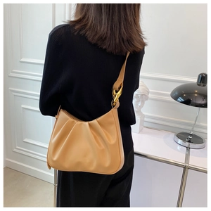 Close-up of pleated beige hobo bag with large gold chain hardware on model's shoulder