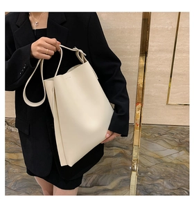 Detailed close-up of a large minimalist cream tote bag on a model in a black suit