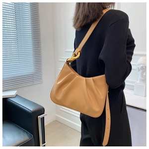 Detailed view of caramel pleated cloud bag with chunky gold chain strap worn by a model