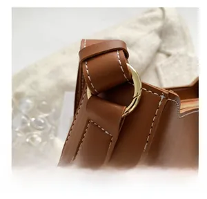 Détail d'un sac en cuir marron avec surpiqûres blanches et boucle en métal doré brillant