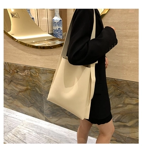 Minimalist beige leather tote bag with wide shoulder strap shown on model in modern interior
