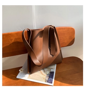Detail of caramel brown leather tote bag with wide strap on dark wooden chair
