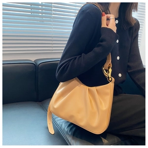 Detailed view of cream-colored pleated cloud bag with golden chain strap on a model