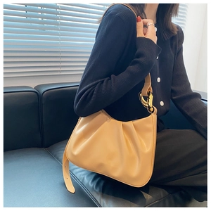 Detail of beige pleated cloud bag with elegant gold chain link strap on leather sofa