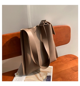 Detail view of a large taupe shoulder tote bag with adjustable wide strap on a wooden bench
