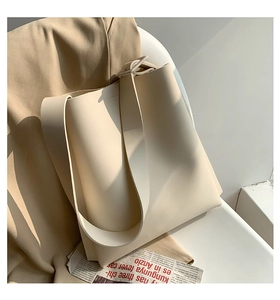 Detail of minimalist cream leather bucket bag with wide shoulder strap and matte finish