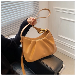 Close-up of camel pleated cloud bucket bag with chunky gold chain strap on leather bench